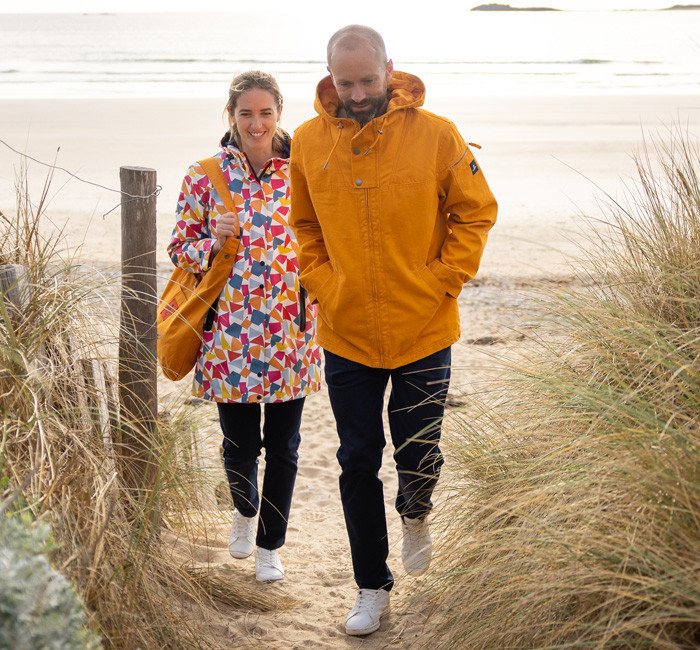 Man wearing a saffron-colored canvas jacket and woman wearing a multicolored tulip-print raincoat with a snap hook